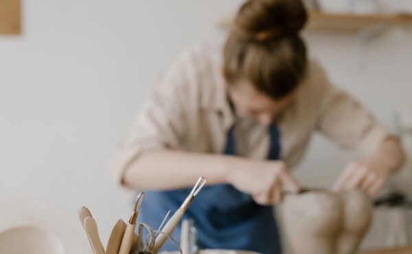 Ein Frau, die Ton formt, mit Töpferwerkzeugen auf einem Arbeitstisch im Vordergrund.